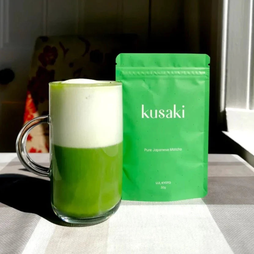 Matcha latte with foam in front of Kusaki matcha pouch