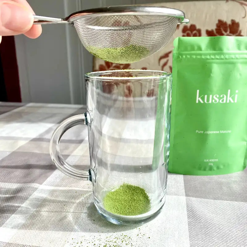 Kusaki Matcha Powder getting sifted into a glass mug with a small sieve